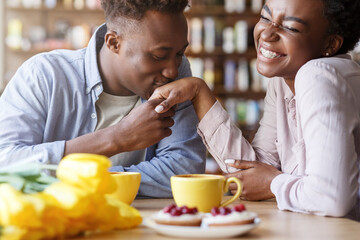 Handsome African American guy kissing his girlfriends hand at coffee shop