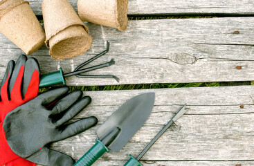 Garden tools, gloves and peat cups for seedlings on a wooden background. Concept image of garden...