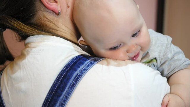 Young mother holds in her arms and kisses her baby on the forehead.