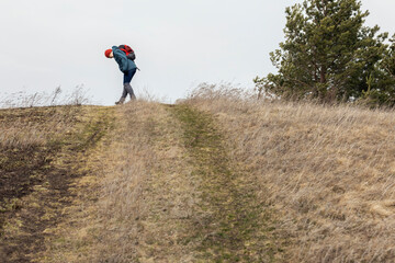 A tourist girl in a sports jacket and hat is walking along a dirt road on a sunny spring day. Hiking, healthy lifestyle.