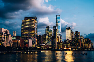 Obraz premium Sceneria widok na panoramę dolnego Manhattanu wieczorem z oświetleniem miasta odbite w rzece Hudson. Piękny widok na panoramę Nowego Jorku. Współczesna metropolia potrzebuje ogromnej ilości prądu