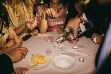 Obraz na płótnie Canvas Elegant people around a table drinking a shot in a night club