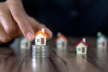 Human hand putting house model on coins stack,  planning savings money of coins to buy a home concept, mortgage and real estate investment.  saving or investment for a house.