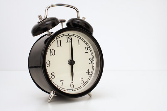 Black vintage alarm clock on table. White background. Wake up concept. An image of a retro clock showing 06:00 pm/am.  