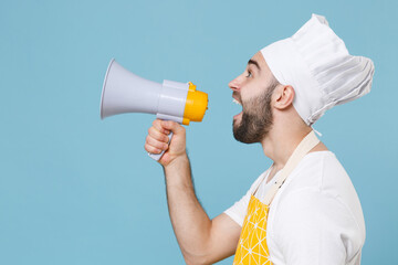 Side view of shocked young bearded male chef or cook baker man in apron white t-shirt toque chefs hat isolated on blue background studio. Cooking food concept. Mock up copy space. Scream in megaphone.