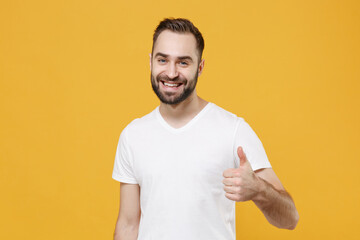 Smiling funny young bearded man guy in white casual t-shirt posing isolated on yellow wall background studio portrait. People sincere emotions lifestyle concept. Mock up copy space. Showing thumb up.