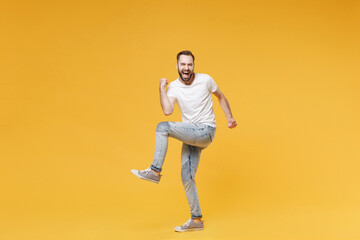 Fototapeta na wymiar Happy young bearded man guy in white casual t-shirt posing isolated on yellow background studio portrait. People sincere emotions lifestyle concept. Mock up copy space. Clenching fists like winner.