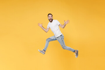 Excited young bearded man guy in white casual t-shirt posing isolated on yellow background studio portrait. People emotions lifestyle concept. Mock up copy space. Jumping spreading hands and legs.