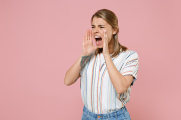 Irritated young blonde woman girl in casual striped shirt posing isolated on pastel pink background studio portrait. People lifestyle concept. Mock up copy space. Scream with hands gesture near mouth.