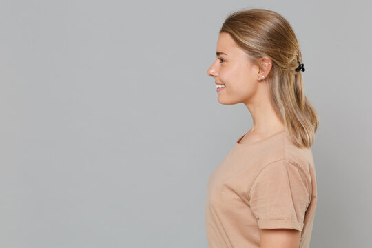 Side view of smiling young blonde woman girl in casual beige t-shirt posing isolated on gray background studio portrait. People sincere emotions lifestyle concept. Mock up copy space. Looking aside.