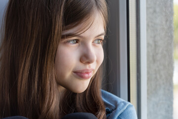 pensive little beautiful brunette girl looks out the window