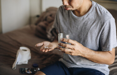 young asian man holding pill and glass water with taking medicine