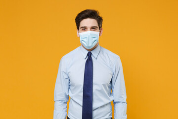 Smiling young business man in classic blue shirt tie sterile face mask isolated on yellow...