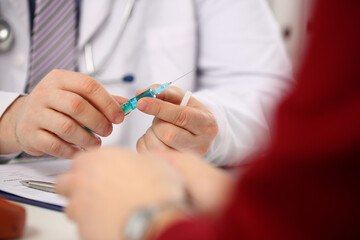 Close up of man physician holding medical syringe with blue liquid while having appointment with patient