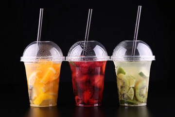 Lemonade to go. Three cups with mint, cherry, strawberry, kiwi, lime, orage, lemon on black background, isolated
