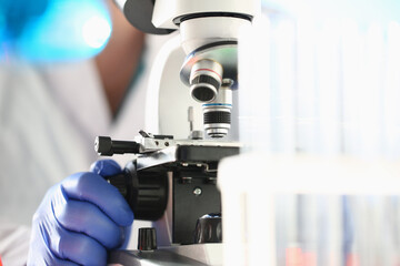 Close up of male researcher in sterile gloves looking at biological samples under microscope
