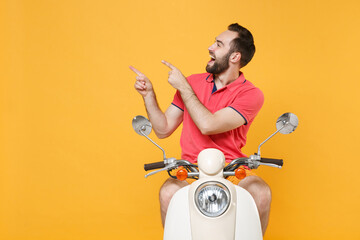 Cheerful young bearded man guy in casual summer clothes driving moped isolated on yellow background studio. Driving motorbike transportation concept. Mock up copy space. Point index fingers aside up.