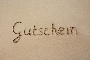 Word coupon written on the sand near the sea.