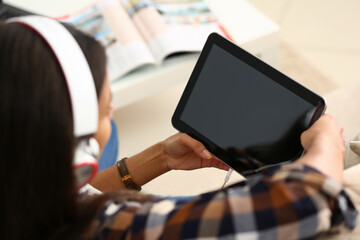 Close up of lady holding electronic pad PC with black display and listening to music through headphones