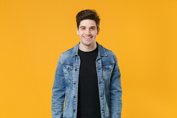 Smiling handsome young man guy wearing casual denim jacket posing isolated on yellow wall background studio portrait. People sincere emotions lifestyle concept. Mock up copy space. Looking camera.