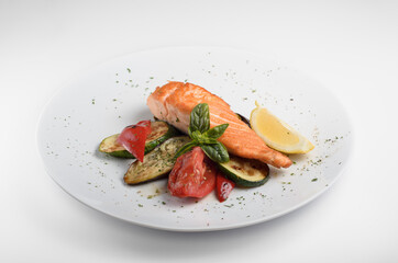 Grilled salmon with vegetables with a beautiful serving on a white plate, a sprig of basil, tomato, a slice of lemon and slices of zucchini grill. For use in menu design and online delivery service.