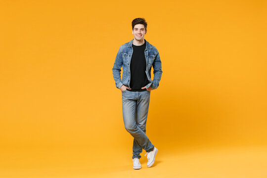 Smiling young man guy 20s wearing casual denim clothes posing isolated on yellow background studio portrait. People sincere emotions lifestyle concept. Mock up copy space. Holding hands in pockets.