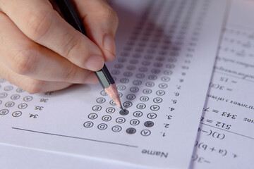 Students hand holding pencil writing selected choice on answer sheets and Mathematics question sheets. students testing doing examination. school exam.