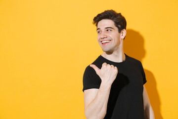 Smiling young man guy 20s wearing casual black t-shirt posing isolated on yellow wall background...