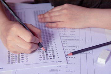 Students hand holding pencil writing selected choice on answer sheets and Mathematics question sheets. students testing doing examination. school exam.