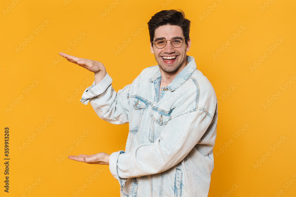 Wall mural Photo of joyful young man in eyeglasses holding copyspace and laughing