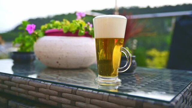 Fresh beer poured into glass on garden table overlooking garden scenery in a shallow depth of field ,blurred background.