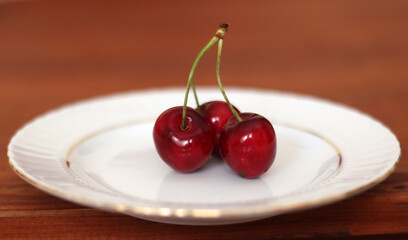 Fresh sour cherries in a wihte plate and green leaves on the board. Fresh ripe sour cherries.