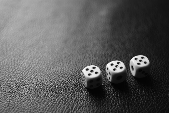 Three dice with fives on a black leather table in corner. Bw photo