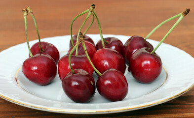 Fresh sour cherries in a wihte plate and green leaves on the board. Fresh ripe sour cherries.
