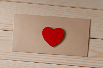 red wooden small heart lies on a brown envelope on wooden table diagonally
