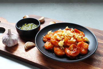Garlic Prawns shrimps fried and spicy seafood sauce are served on the wooden holder on the grey table in the restaurant