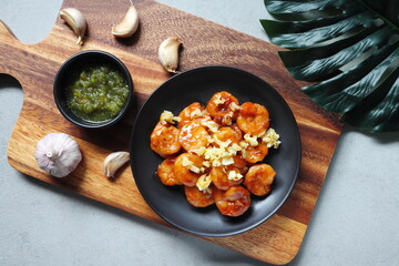Garlic Prawns shrimps fried and spicy seafood sauce are served on the wooden holder on the grey table in the restaurant
