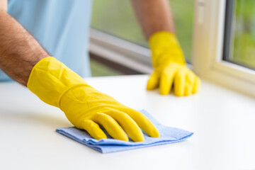 Close up of hands in rubber protective yellow gloves cleaning the white surface with a rag. Home, housekeeping concept