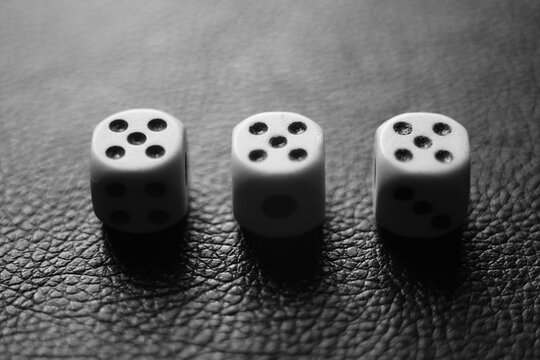 Three dice with fives on a black leather table. Bw photo
