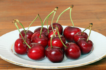 Fresh sour cherries in a wihte plate and green leaves on the board. Fresh ripe sour cherries.
