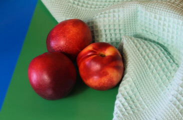 Three nectarines next to a towel on a green and blue background.