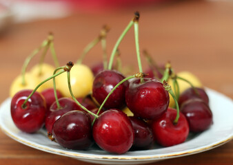 Fresh sour cherries in a wihte plate and green leaves on the board. Fresh ripe sour cherries.