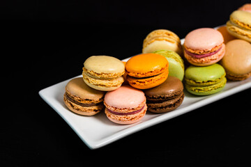 Colorful Macaroons Chocolate, Pistachio, Cherry, Orange, Vanilla Flavor Background on Black Background. Selective focus.