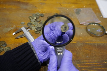archaeologist checking coins with a magnifying glass. archeology background.  Archeology Museum