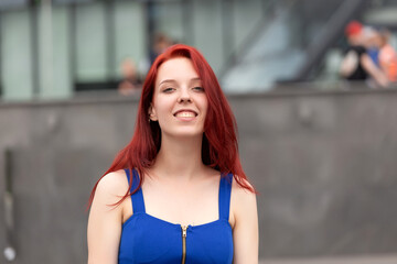 Pretty young woman with a wonderful sense of humor, red hair and a blue dress on a city street laughing at the camera