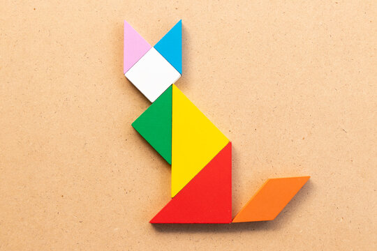 Color tangram puzzle in sitting cat shape on wood bacground