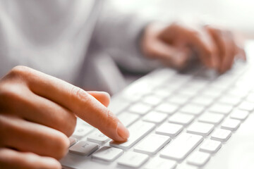 female hand presses enter key on white keyboard, top view
