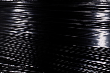 Texture of a stretched plastic film on a black background, food rumpled cellophane wrap - obrazy, fototapety, plakaty