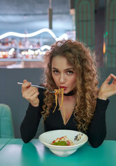Cute girl with curly hair eating pasta in a restaurant