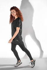 Isolated slender red-haired curly-haired girl in leggings and a T-shirt on a white background. A happy girl in a jump. Levitating girl snipe shot.